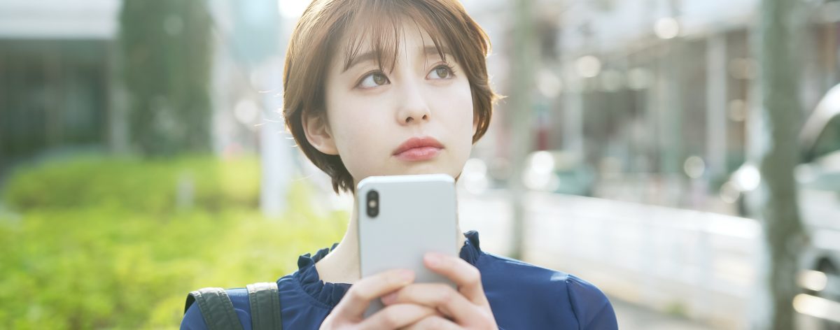 スマートフォンを持って考え事をする女性