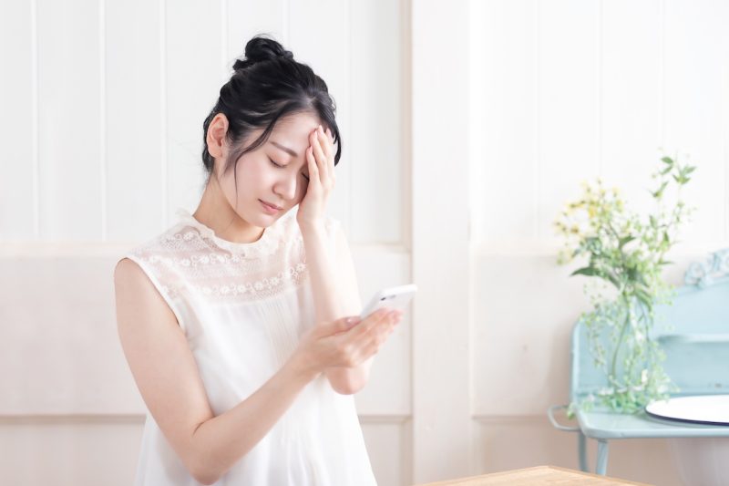 スマホで悪いメッセージを受け取って悲しむ女性