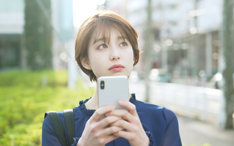 スマートフォンを持って考え事をする女性